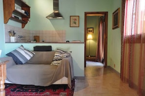 A cozy room with a sofa, a kitchen area with a tiled backsplash, and a hallway leading to another room. - Holiday home with panoramic views and pool (Vicchio)