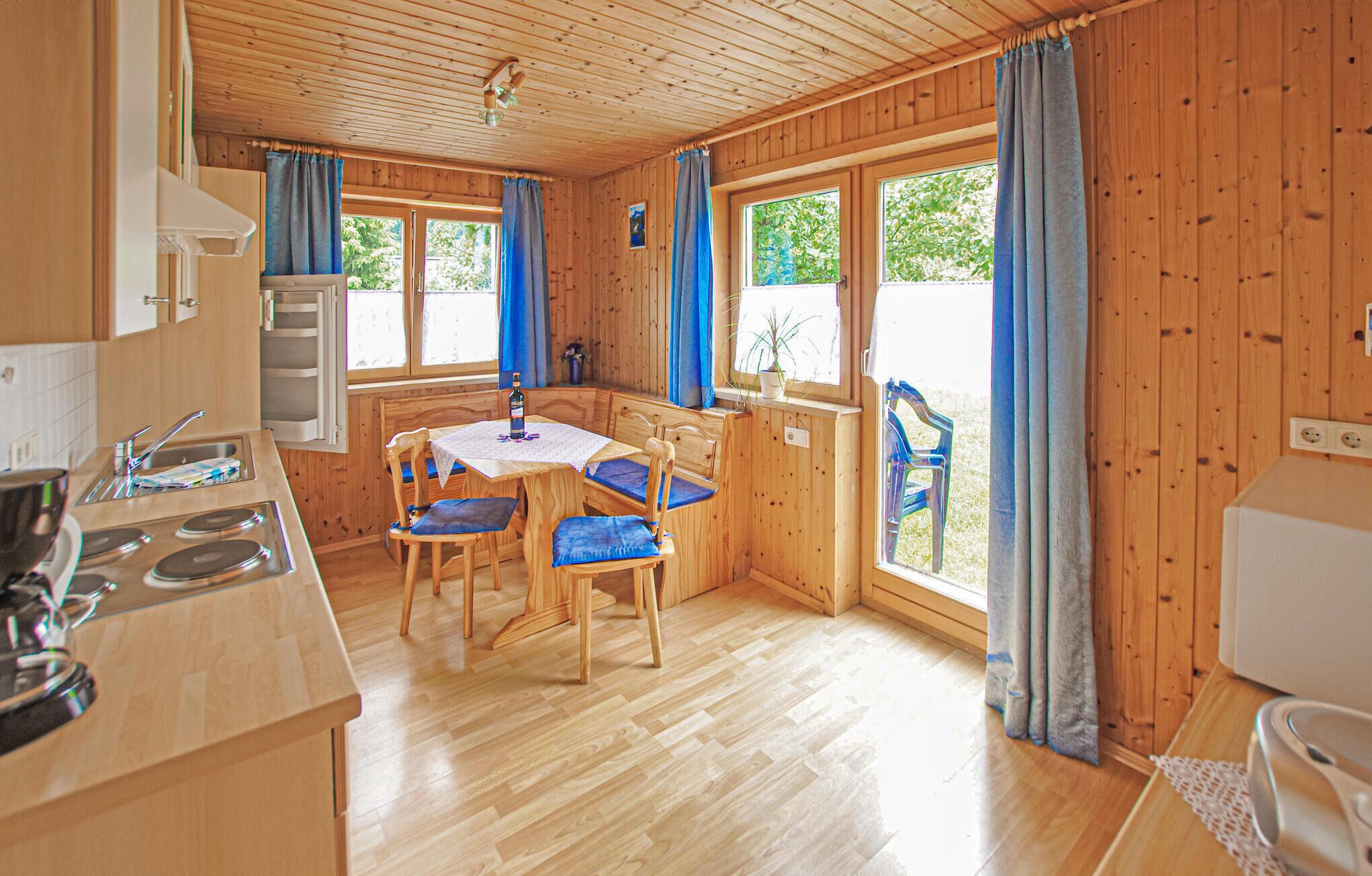 A wooden cabin with a kitchen, dining area, and a window overlooking greenery.