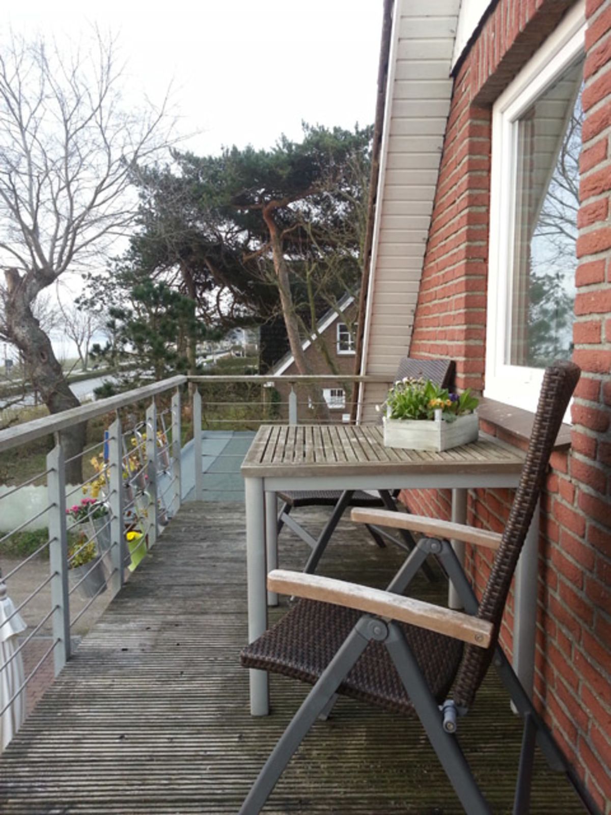 A wooden deck with a table and chairs, a railing, and a brick wall.