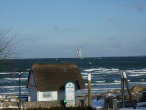 A coastal building with a thatched roof, a signboard, and a view of the sea with a kite surfer in the distance.