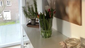 Eine moderne Küche mit einem großen Fenster, einem Blumentopf, einer Blumenvase und einem Bild an der Wand.