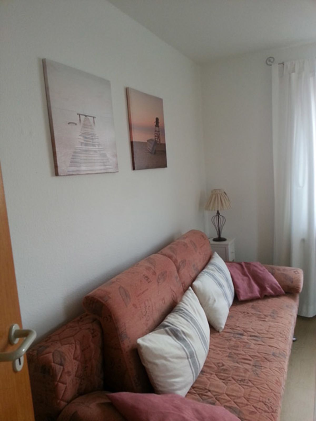 Una habitación con un sofá, dos cuadros en la pared, una lámpara y una puerta.