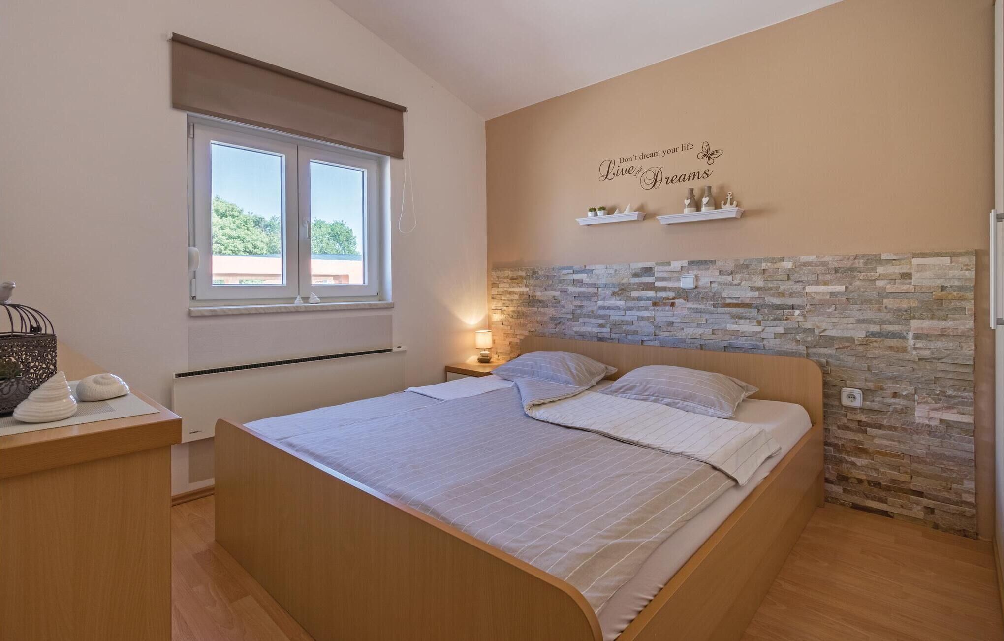 Una camera da letto con un letto, un comodino, una finestra con persiana, una parete con decorazioni in pietra e una mensola con oggetti decorativi.