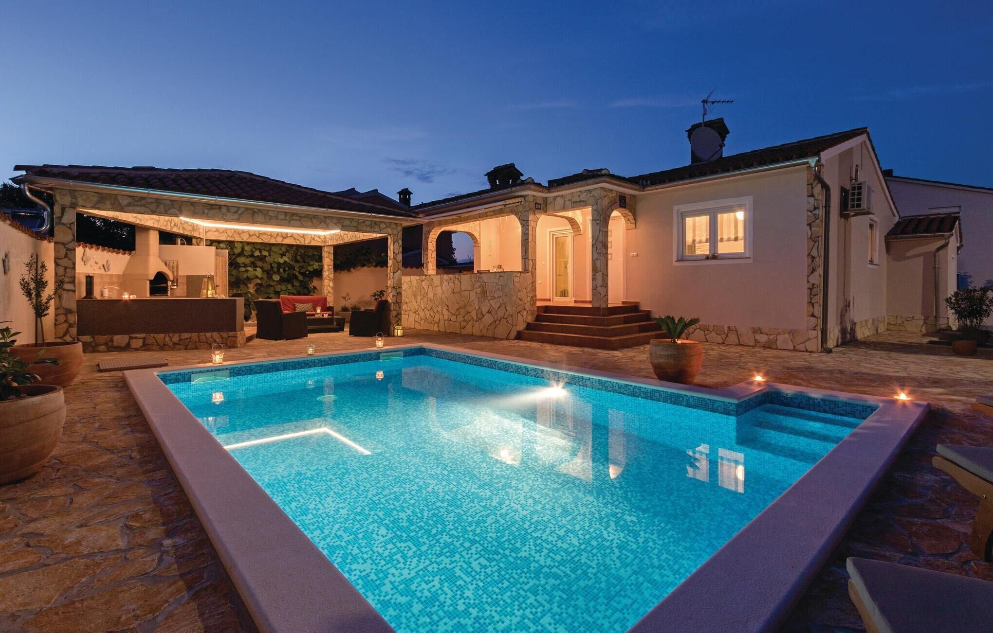 A swimming pool with a stone deck, a covered patio with seating, and a stone wall.