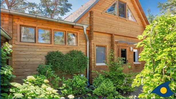 Eine Holzhütte mit geneigtem Dach, großen Fenstern und einem Garten mit verschiedenen Pflanzen.