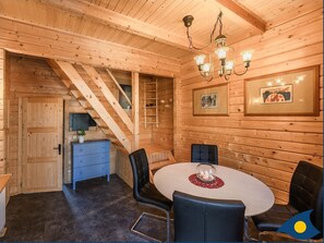 Interior de uma cabana de madeira com área de jantar, escada e pequena cozinha.