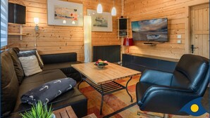 Ein gemütlicher Raum im Chalet-Stil mit Holzwänden, einem großen an der Wand befestigten Fernseher, einem Holztisch, einer Couch und einem Sessel.