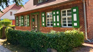 Una casa tradicional de ladrillo con contraventanas verdes, techo inclinado y chimenea de ladrillo.