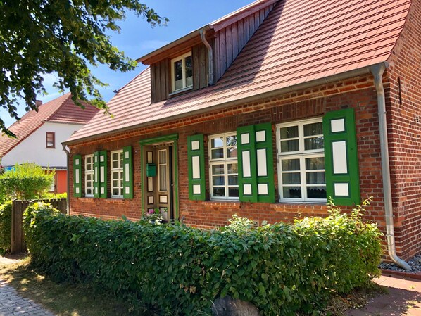 A traditional brick house with green shutters, a sloped roof, and a brick chimney.