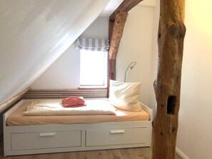 Een slaapkamer in loftstijl met een schuine hemel, een raam met gestreept gordijn, een bedlamp en een houten balkenstructuur.