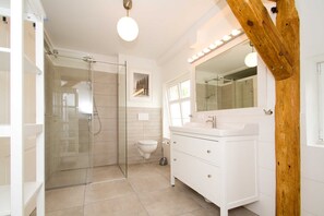 Een badkamer met een douchecabine van glas, toilet, wastafel met spiegel en een houten balkenconstructie.