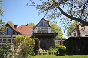 Een huis met twee verdiepingen, een balkon, een tuin met potplanten en een houten omheining.