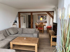 A living room with a sofa, a wooden coffee table, and a dining area with a table and chairs. - Captain's deck - vacation apartment in the captain's house (Wustrow)
