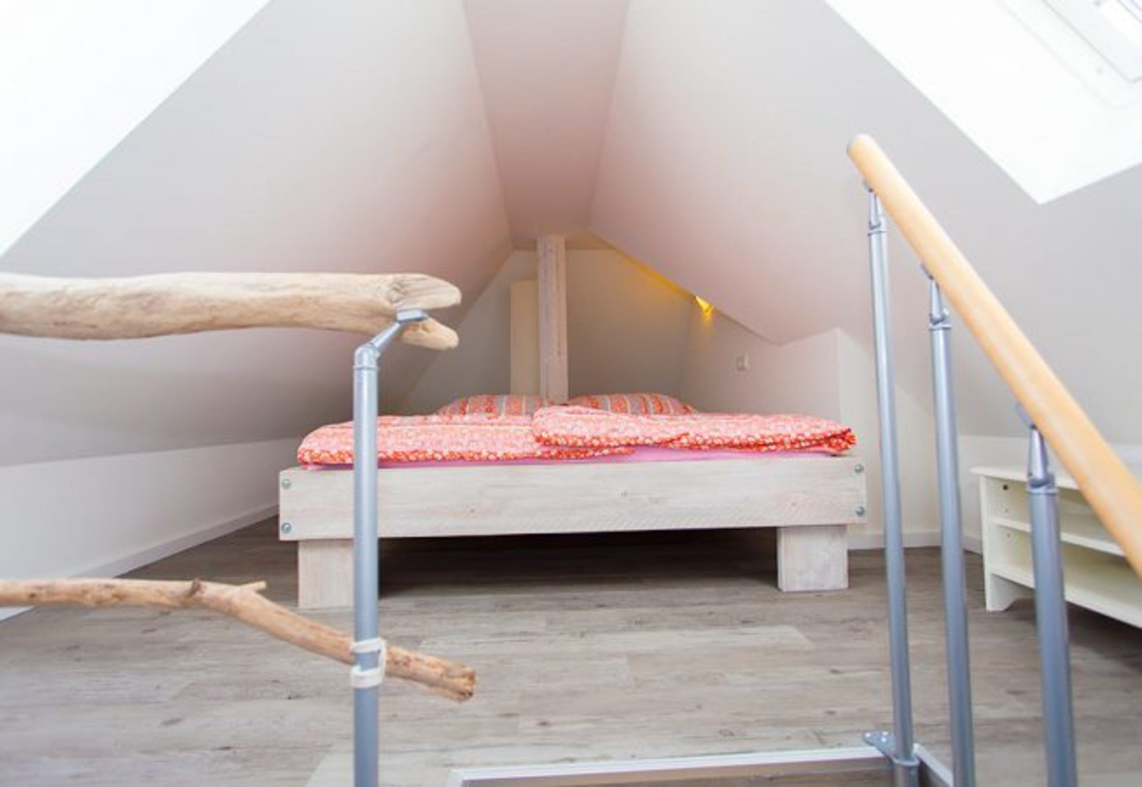 Ein kleines, dreieckiges Schlafzimmer im Dachgeschoss mit Bett, Holzbalken und einem Dachfenster.
