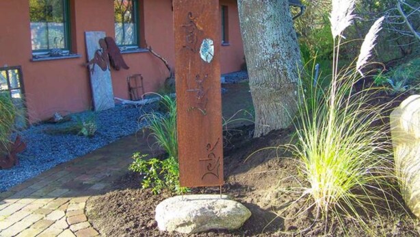A rustic wooden sign with carvings, a stone pathway, and a tree in a garden setting. - Vacation apartment Richard - Holiday home at the Museumshof (Zirkow)