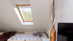 A bedroom with a sloped ceiling, a bed with a star-patterned bedspread, a bedside table with a decorative vase, and a window providing natural light. - Vacation apartment Richard - Holiday home at the Museumshof (Zirkow)