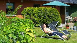 A garden with two lounge chairs and a green umbrella. - Vacation apartment Richard - Holiday home at the Museumshof (Zirkow)