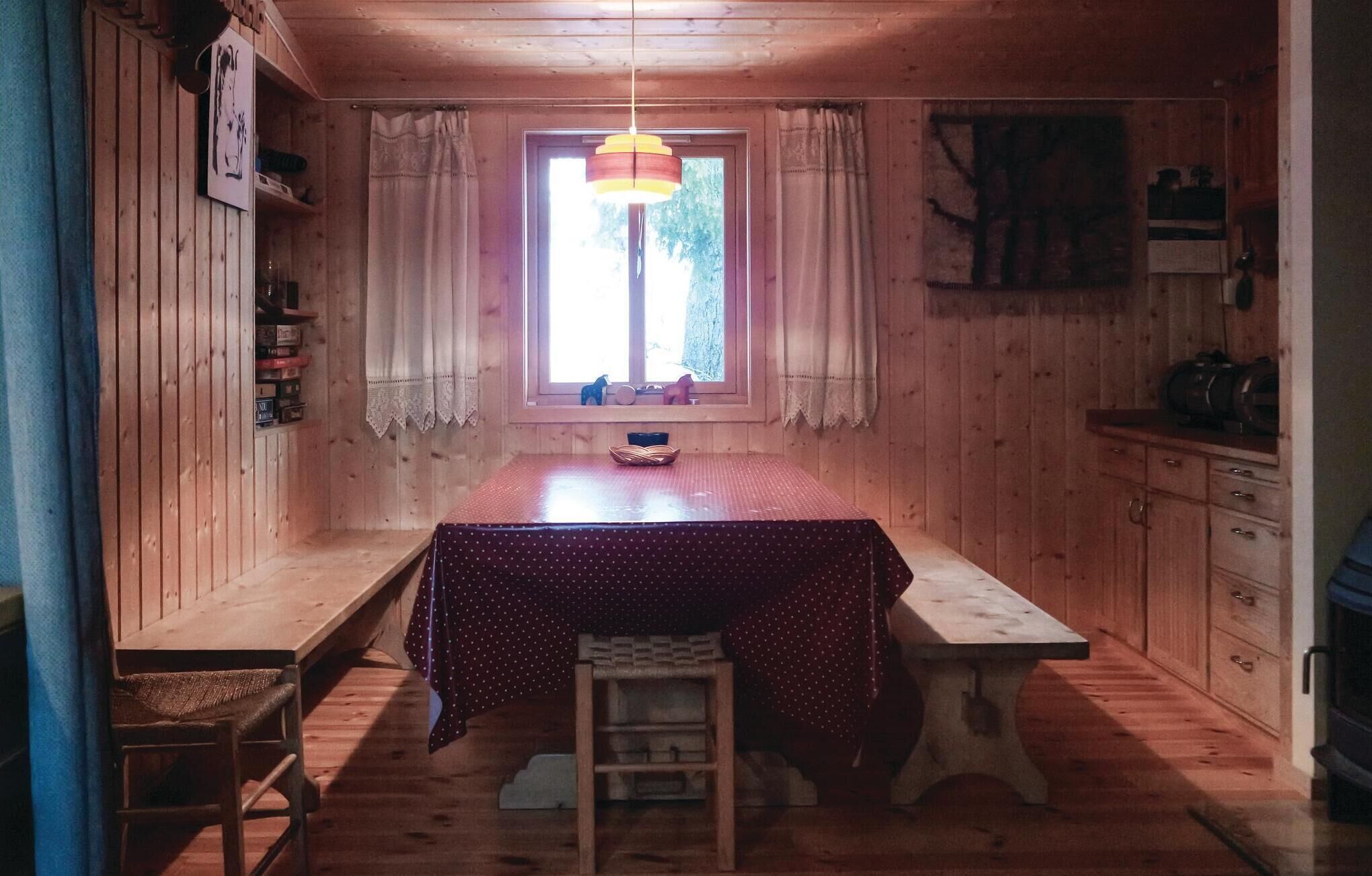 L’intérieur d’un chalet chaleureux, avec une table à manger en bois, un banc et une fenêtre agrémentée de rideaux.