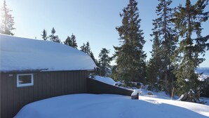 A snow-covered house with a wooden exterior, surrounded by tall evergreen trees and a clear blue sky. - Gorgeous home in Sjusjøen with sauna (Sjusjøen)