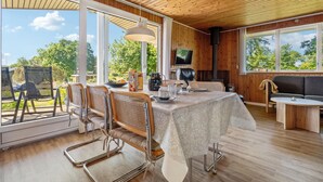 A dining area with a table set for four, a television mounted on the wall, and a large window offering a view of the outdoors. - 3 bedroom gorgeous home in Hejls (Hejls)
