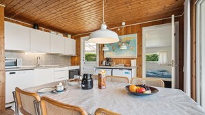 A modern kitchen with white cabinets, a dining table with wicker chairs, and a large window. - 3 bedroom gorgeous home in Hejls (Hejls)