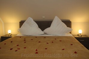 A bed with rose petals, two bedside lamps, and a headboard.
