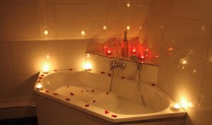 Eine Wanne mit Rosenblüten, Kerzen und einer Flasche.