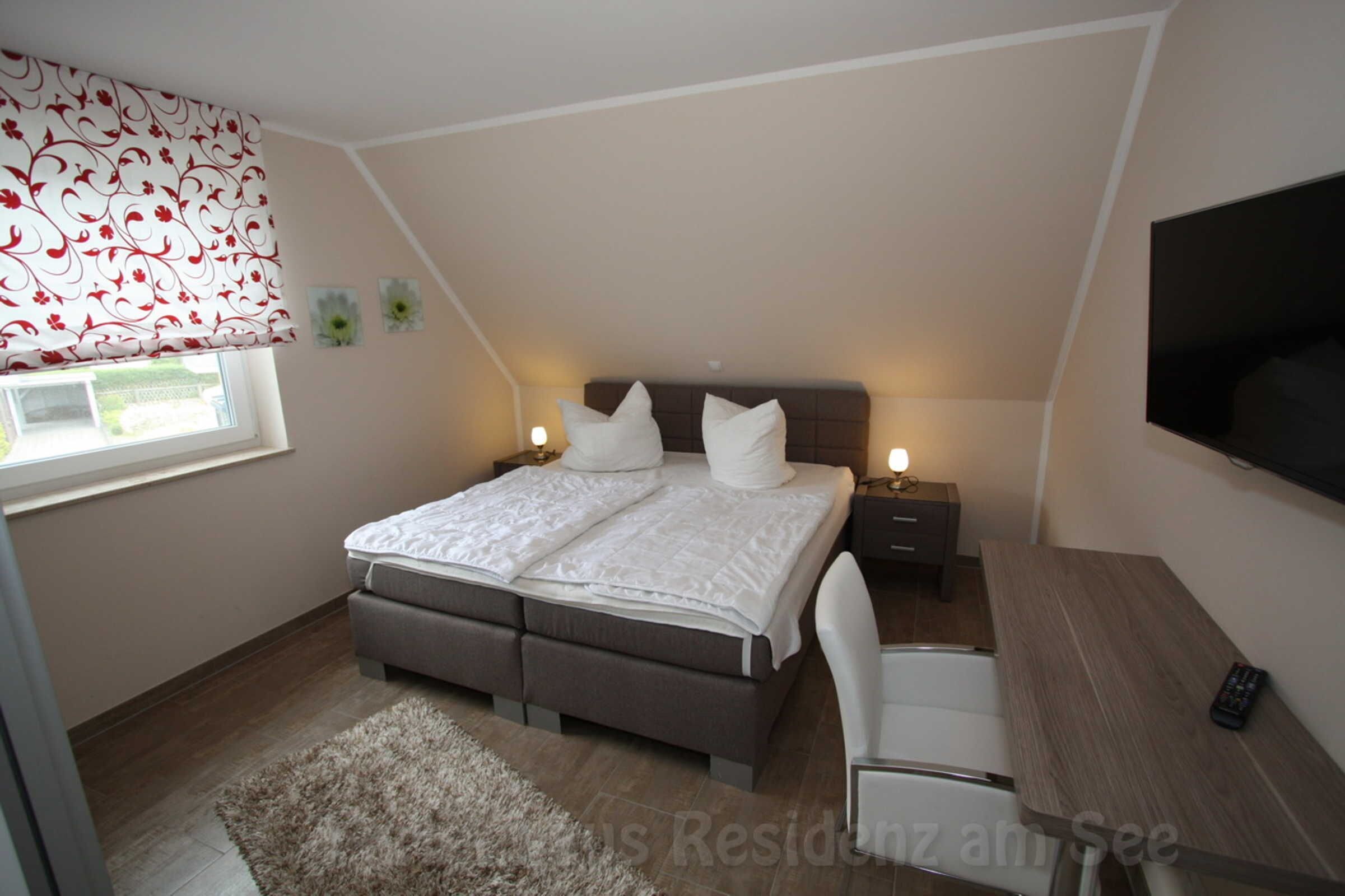 A bedroom with a bed, bedside tables, a desk, and a TV.