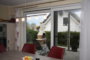A modern kitchen with a built-in oven, a dining area with a table and chairs, and a view of a garden and outdoor seating area.
