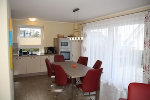 A dining area with a table and chairs, a kitchen in the background, and a window with curtains. - Vacation home Residenz am See - Holiday home Residenz am See (50 meters from the (Göhren-Lebbin)