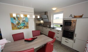 Une cuisine moderne avec un coin repas, agrémentée d’un tableau, de chaises rouges et d’un four encastré.
