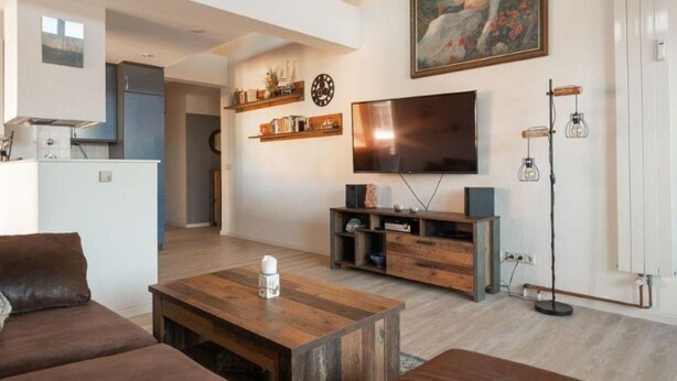 Un salon moderne avec une table basse en bois, des canapés marron, un téléviseur à écran plat et un tableau accroché au mur.