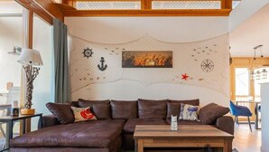 Un salon chaleureux avec un canapé d’angle en cuir marron, une table basse en bois et un mur décoratif orné d’une boussole et d’un tableau.