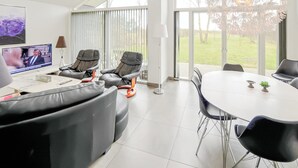 Een moderne woonkamer met een televisie, leren banken, een eettafel en grote ramen.