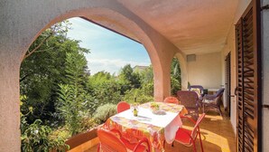 Een terras buiten, met een tafel gedekt voor twee personen, omringd door rode stoelen, onder een stenen boog.