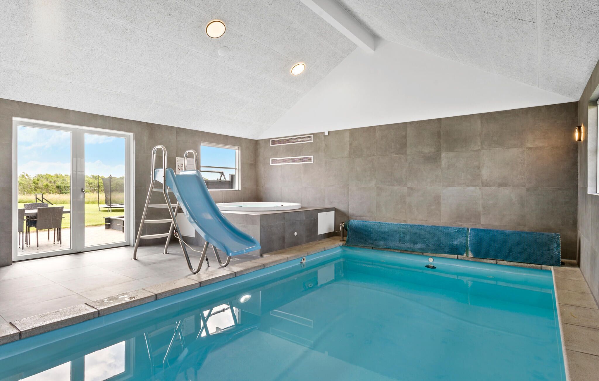 Una piscina coperta con uno scivolo, una vasca idromassaggio e vista sull'esterno.