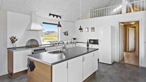A modern kitchen with a large island, a built-in oven, and a window overlooking a garden. - Cozy home in Løkken with WiFi (Løkken)
