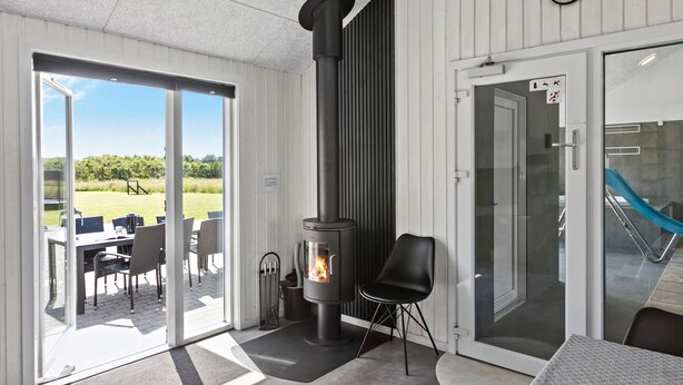 A modern room with a wood-burning stove, a dining area with outdoor seating, and a view of a green landscape. - Cozy home in Løkken with WiFi (Løkken)