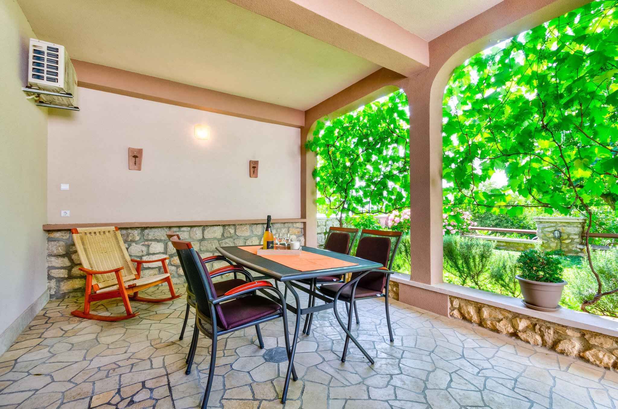 Eine Terrasse mit Tisch und Stühlen, einem Steinboden und Blick ins Grüne durch einen Bogen.