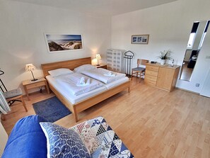 A bedroom with a wooden bed, bedside tables with lamps, a desk, a chair, and a dresser.