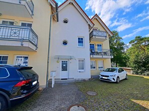 A multi-story residential building with a central entrance, balconies, and a paved driveway.