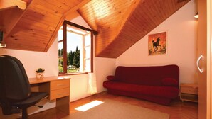 A room with a wooden ceiling, a desk with a chair, a red sofa, and a window with a view of trees.