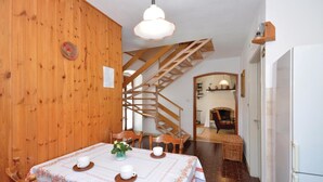 A wooden interior with a dining table set for two, a spiral staircase, and a kitchen area with a refrigerator.