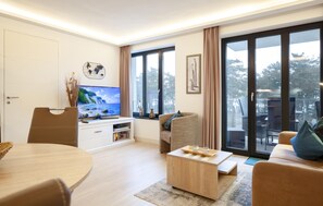 A modern living room with a flat-screen TV, a dining table, a sofa, and a coffee table. - Lovely apartment in Binz with outdoor swimming pool (Prora/Rügen)