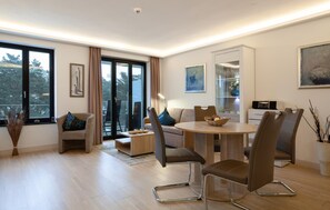 A modern living room with a dining table, sofas, and a glass door leading to an outdoor area. - Lovely apartment in Binz with outdoor swimming pool (Prora/Rügen)