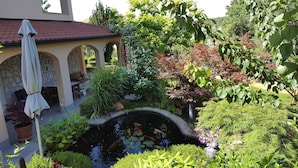 Ein Garten mit Teich, Gartenmöbeln und einer überdachten Sitzgelegenheit.