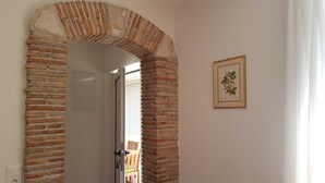 Ein rundbogiger Backsteinbogen führt zu einem Raum, an dessen Wand eine gerahmte Pflanzenillustration hängt.