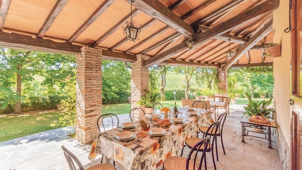 Une terrasse extérieure couverte, avec une table en pierre dressée pour les repas, entourée de chaises et d’un pilier en briques.