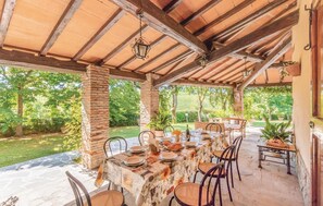 An outdoor covered patio with a stone table set for dining, surrounded by chairs and a brick pillar. - Gorgeous home in Terranuova B.ni AR (Terranuova B.ni AR)