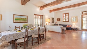 Un coin repas avec une table dressée pour quatre personnes, des poutres en bois au plafond et un canapé à l’arrière-plan.